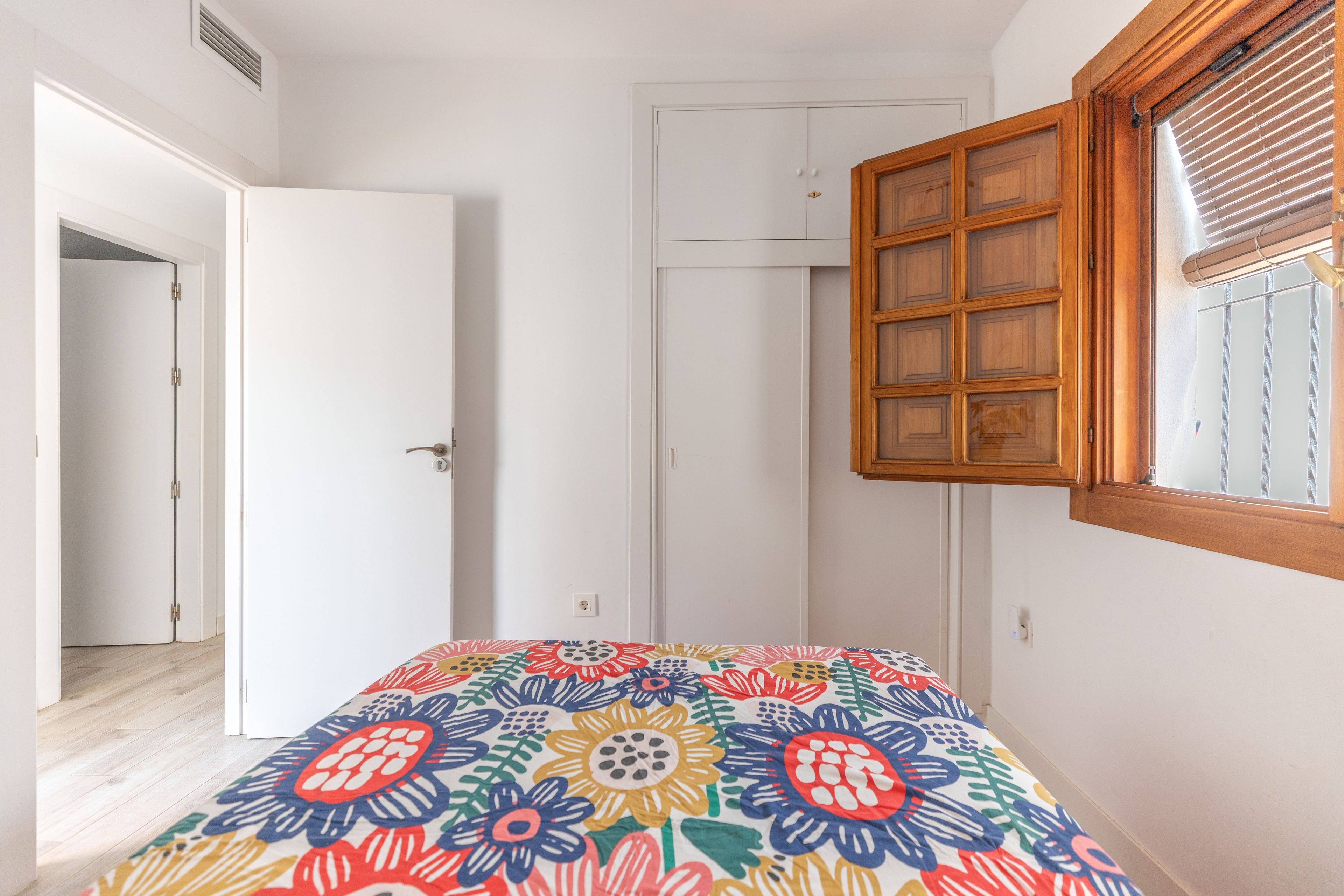 A bedroom with a bed, a wardrobe, a window with blinds, and a door.