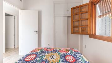 A bedroom with a bed, a wardrobe, a window with blinds, and a door.
