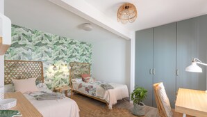 A bedroom with two beds, a wardrobe, a desk, a chair, and a hanging light fixture.