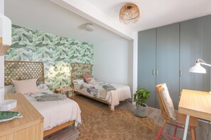 A bedroom with two beds, a wardrobe, a desk, a chair, and a hanging light fixture.