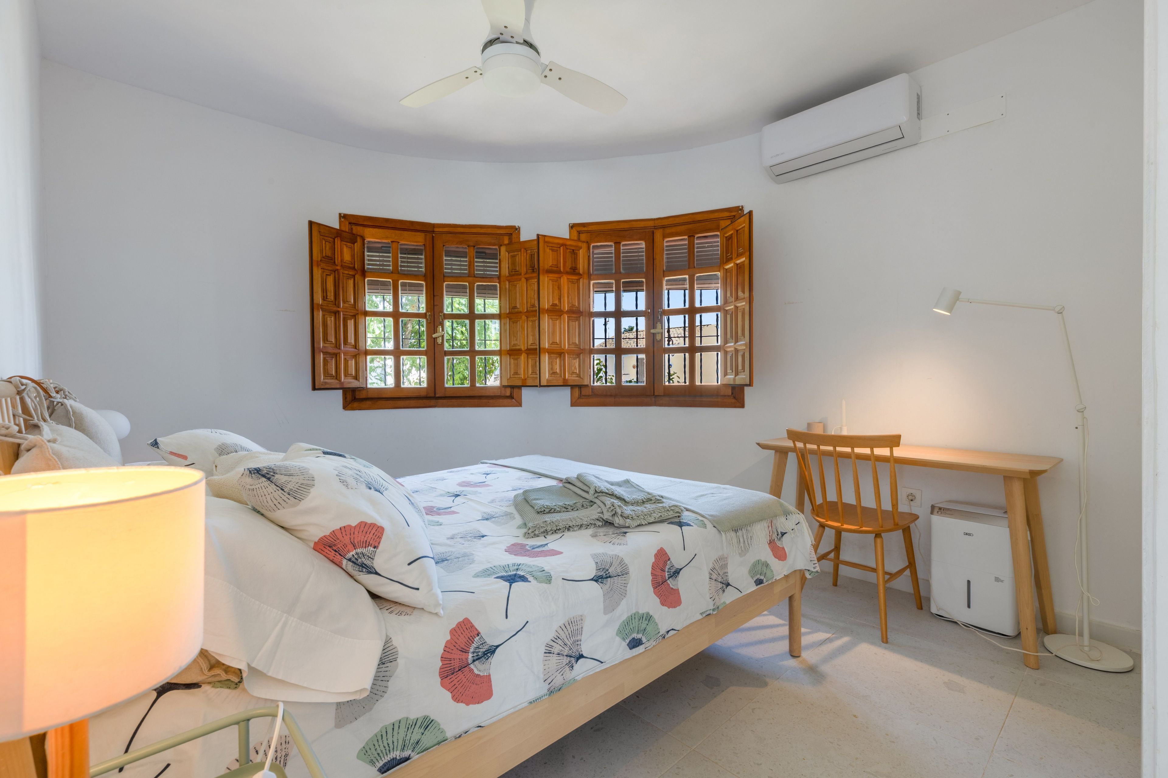 Ein Schlafzimmer mit einem Bett, einem Schreibtisch, einem Stuhl, einer Lampe und einem Deckenventilator.