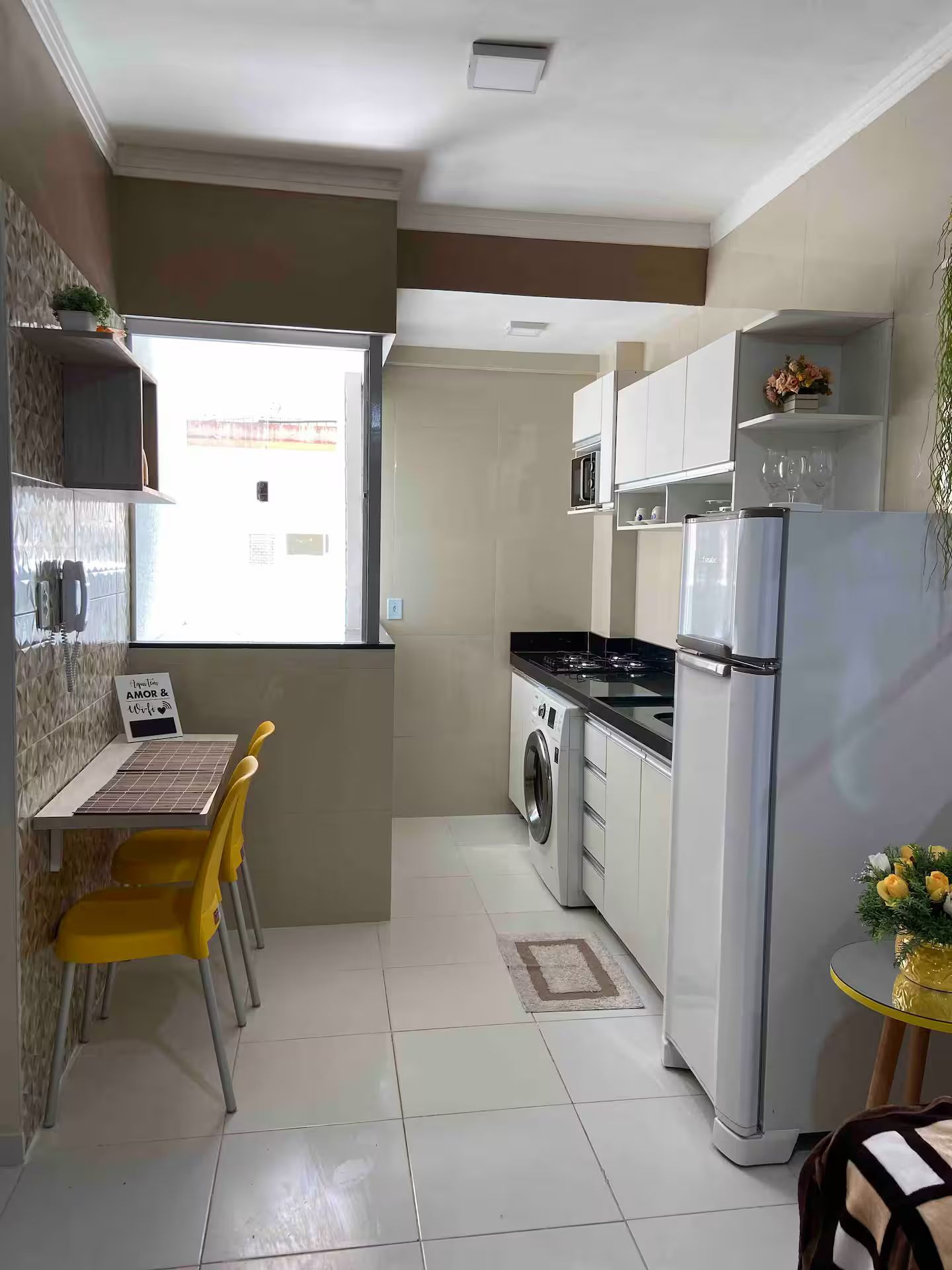 A compact kitchen with a washing machine, a refrigerator, and a dining area with a chair and table.