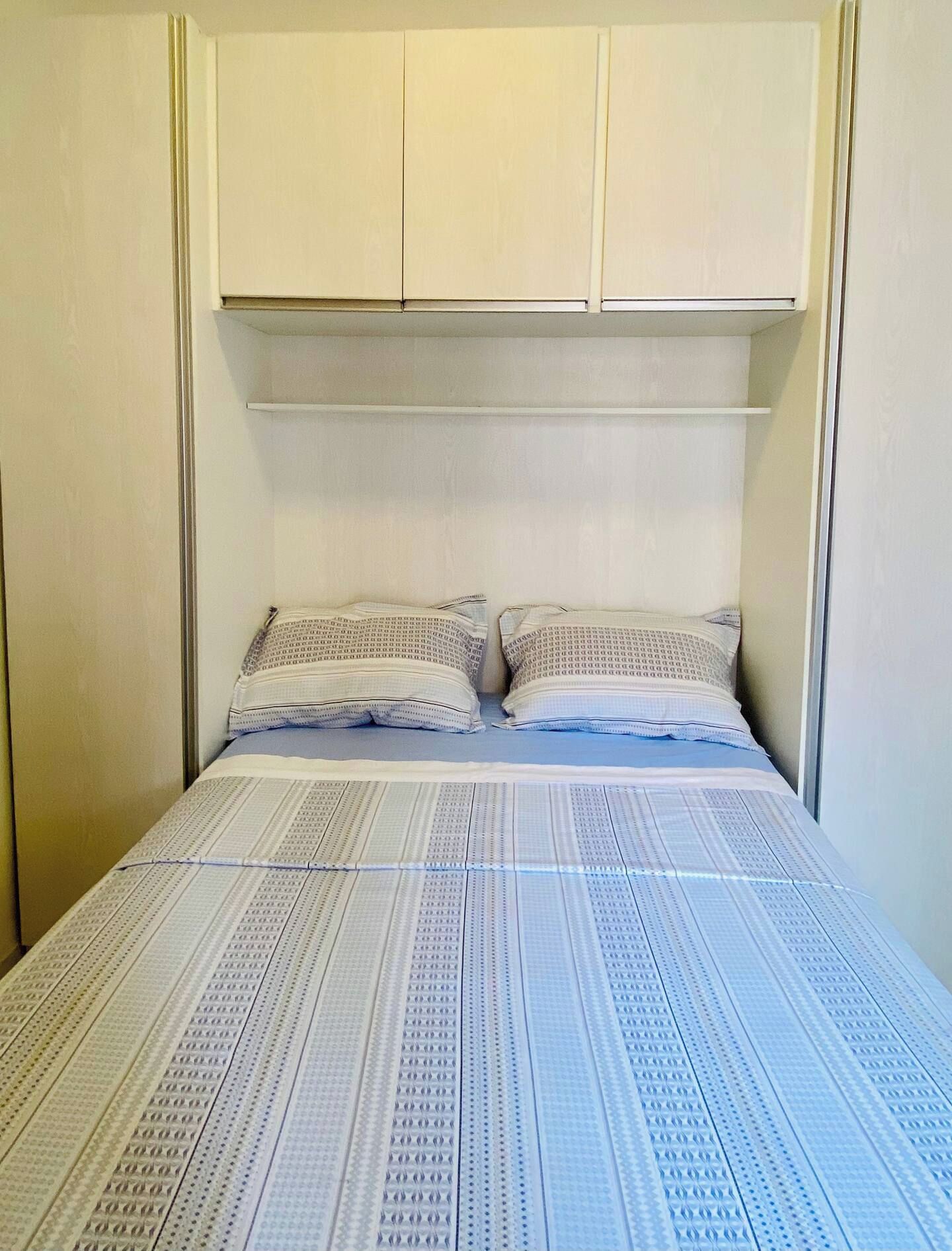 Un dormitorio con cama, dos almohadas y cabecera con espacio de almacenamiento.