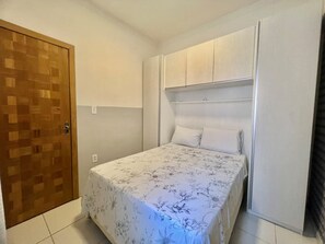 Un dormitori amb un llit, una porta de fusta i un armari blanc.