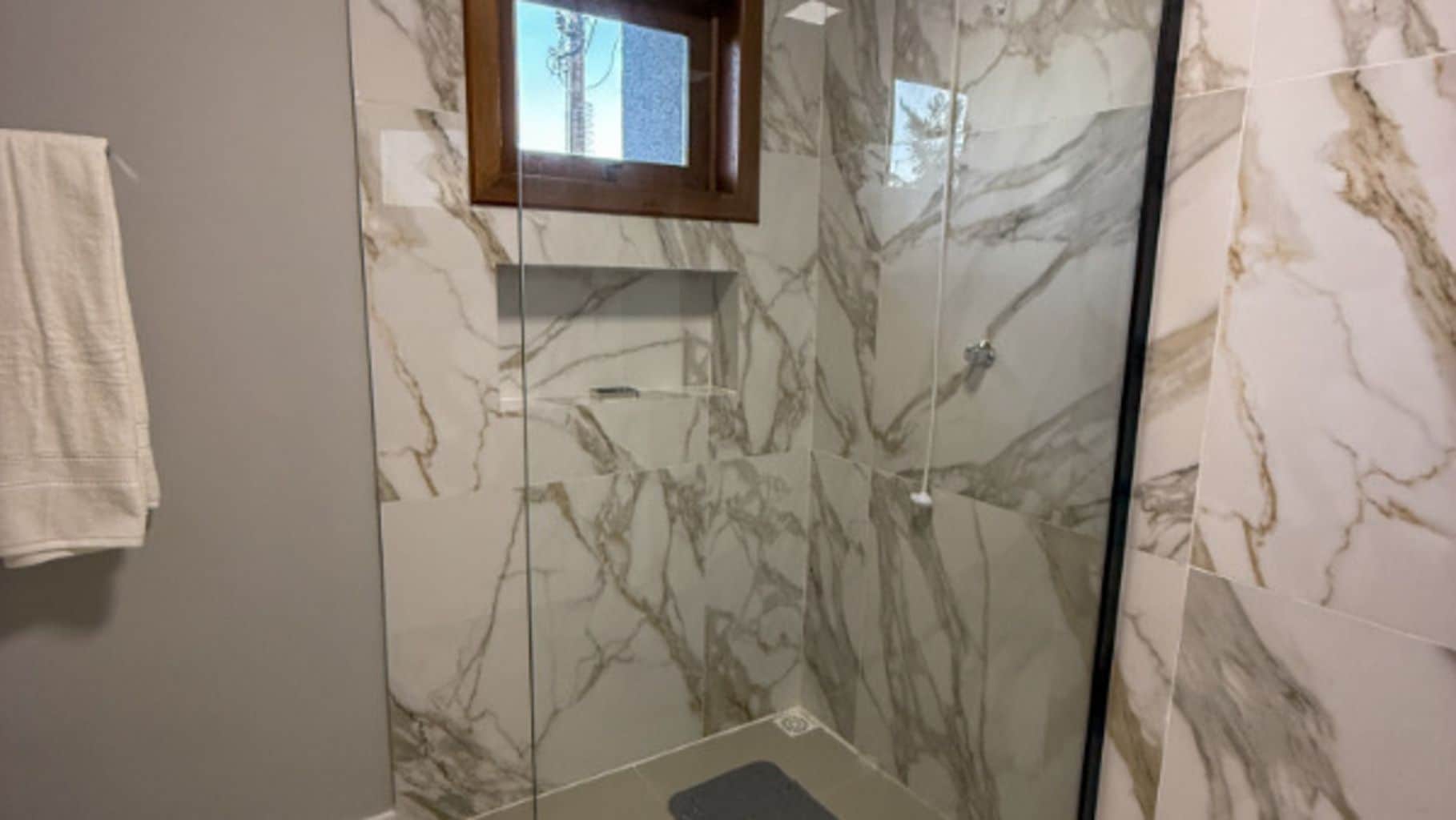 A bathroom with marble walls, a glass shower enclosure, and a small window.