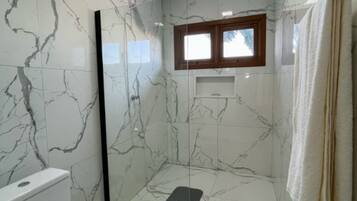 A bathroom with marble walls, a window, and a shower area.
