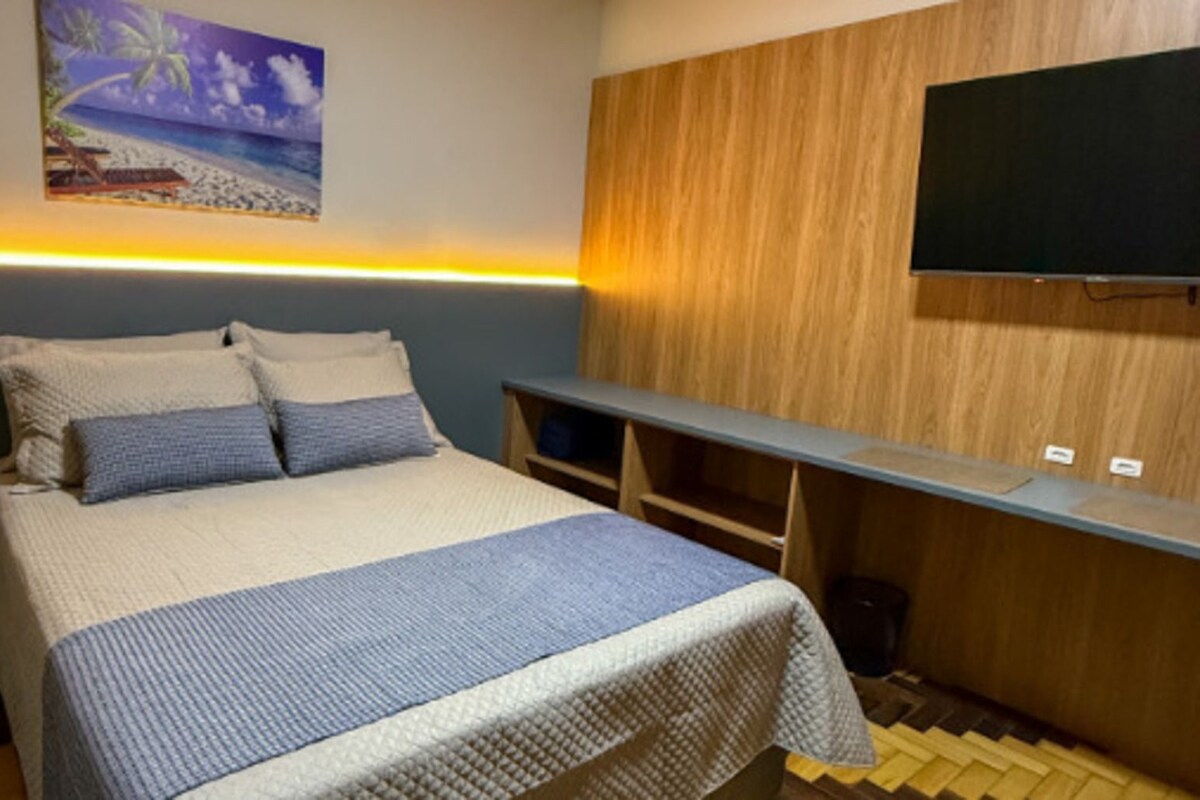 Un dormitori amb un llit, una tauleta de nit, un televisor fixat a la paret i un disseny de panells de fusta.