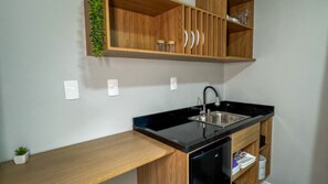 Una cocina con encimera negra, armarios de madera, un lavamanos de acero inoxidable y una pequeña planta en maceta.