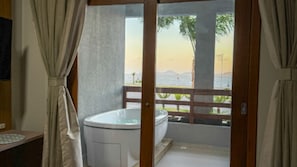 Habitación con bañera y vista al mar desde un balcón de madera.