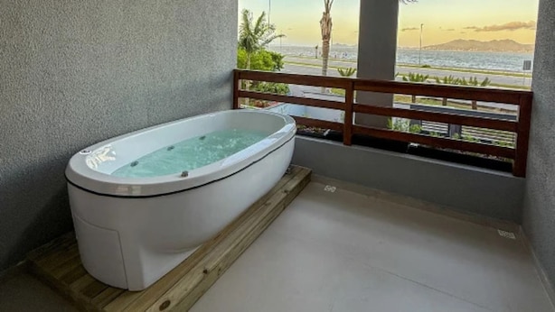 A spa area with a hot tub, wooden deck, and a view of the sea. - Casa Ponte Floripa (Florianópolis)
