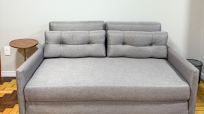 Un sofá gris con una mesita de madera y una pequeña mesa redonda.