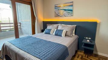 A bedroom with a bed, a nightstand, a painting, and a view through a door.