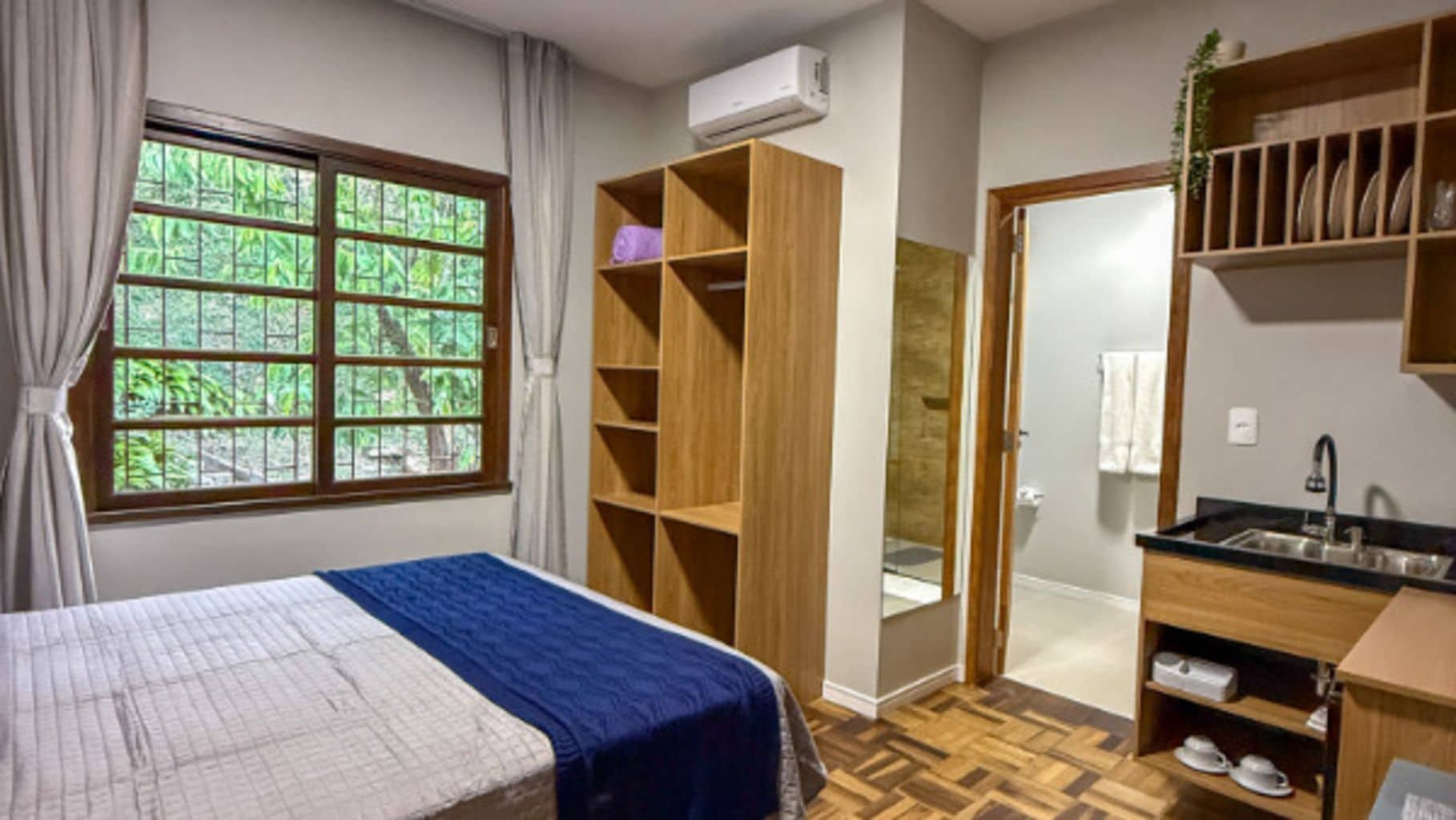 A bedroom with a bed, a wardrobe, a bathroom, and a kitchenette.