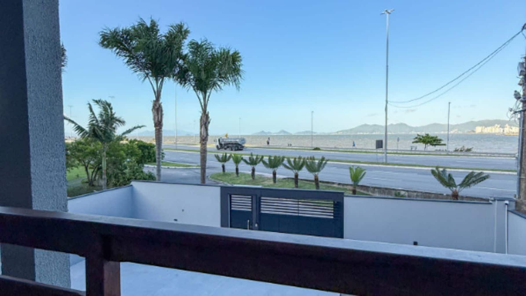 Varanda com vista para uma estrada, palmeiras e um corpo d'água ao longe.