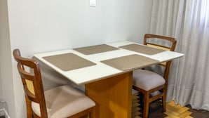 A dining table with four square placemats, two wooden chairs with cushioned seats, and a white wall with a light switch. - Casa Ponte Floripa (Florianópolis)
