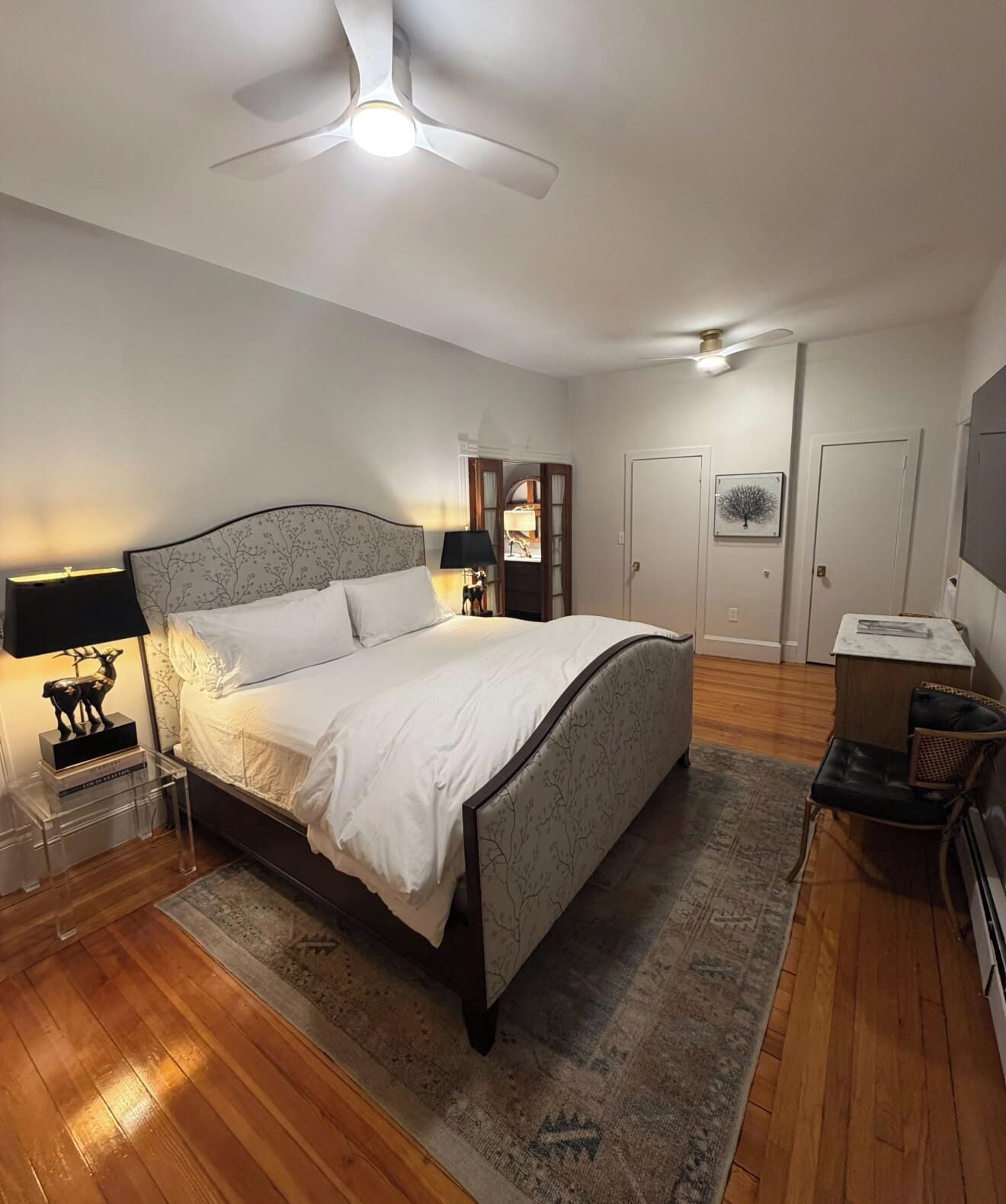 Une chambre à coucher avec un lit, une table de chevet, une lampe, un ventilateur de plafond et une porte.