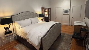 Un dormitorio con una cama, una mesita de noche, una lámpara, un ventilador de techo y una puerta.
