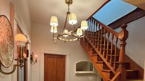 Una escalera de madera con barandilla, un candelabro con varias luces y una puerta al final.