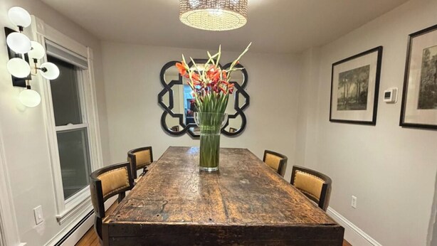 Un comedor con una mesa de madera, seis sillas, un jarrón con flores, una araña y cuadros enmarcados en la pared.