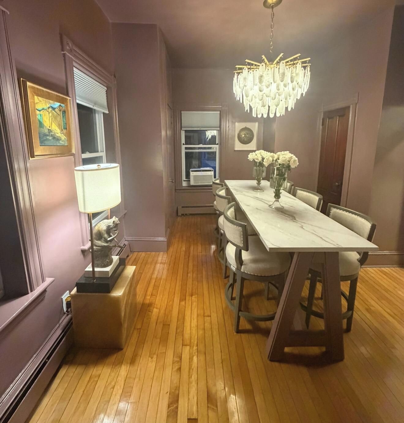 A dining area with a marble table, chairs, a chandelier, and a window with blinds.