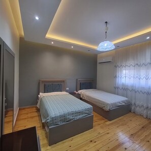 A bedroom with two beds, wooden flooring, a ceiling light fixture, and an air conditioning unit. -  Luxurious 270m Apartment in Nasr City (Cairo Governorate)