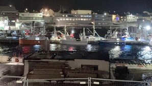 A nighttime harbor with boats docked, a building with illuminated windows, and a waterfront promenade.