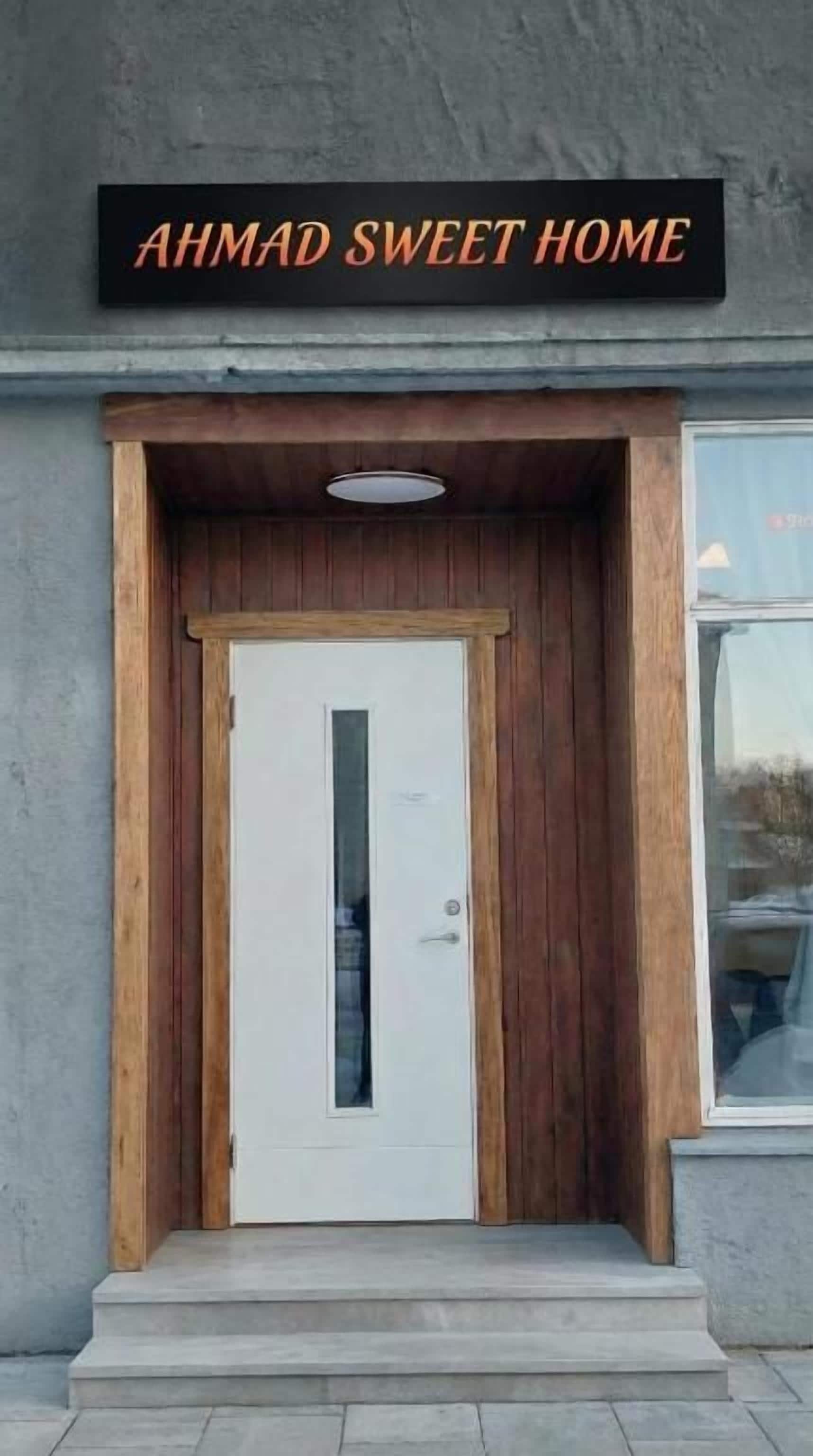 Ein Gebäudeeingang mit einem Schild, auf dem 'AHMAD SWEET HOME' steht, über einer weißen Tür mit einem kleinen Fenster.