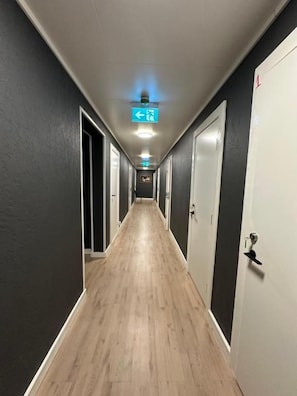 Un pasillo con puertas a ambos lados, una lámpara en el techo y un letrero de indicaciones.