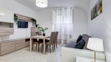 Ein moderner Wohnraum mit Essbereich, einer Couch und einem an der Wand befestigten Fernseher.