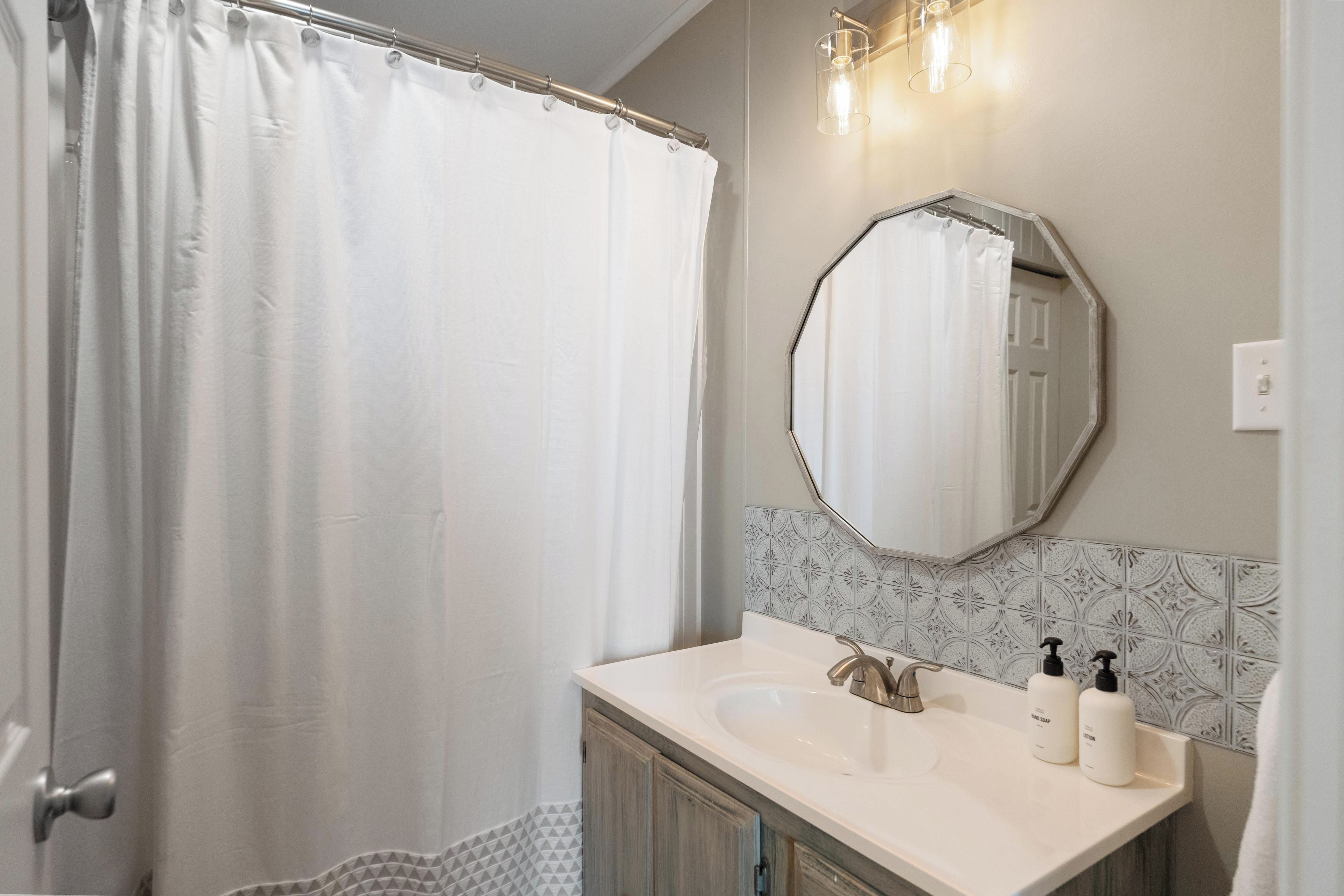 A bathroom with a shower curtain, a sink with a faucet, and two bottles of hand soap.