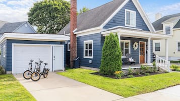 A two-story house with a garage, a chimney, and a front porch with a small tree and a wreath.
