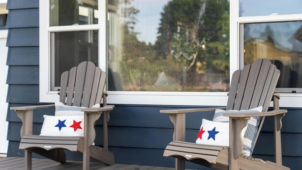 Two Adirondack chairs with star-patterned cushions on a wooden deck, positioned in front of a house with dark siding and white trim.