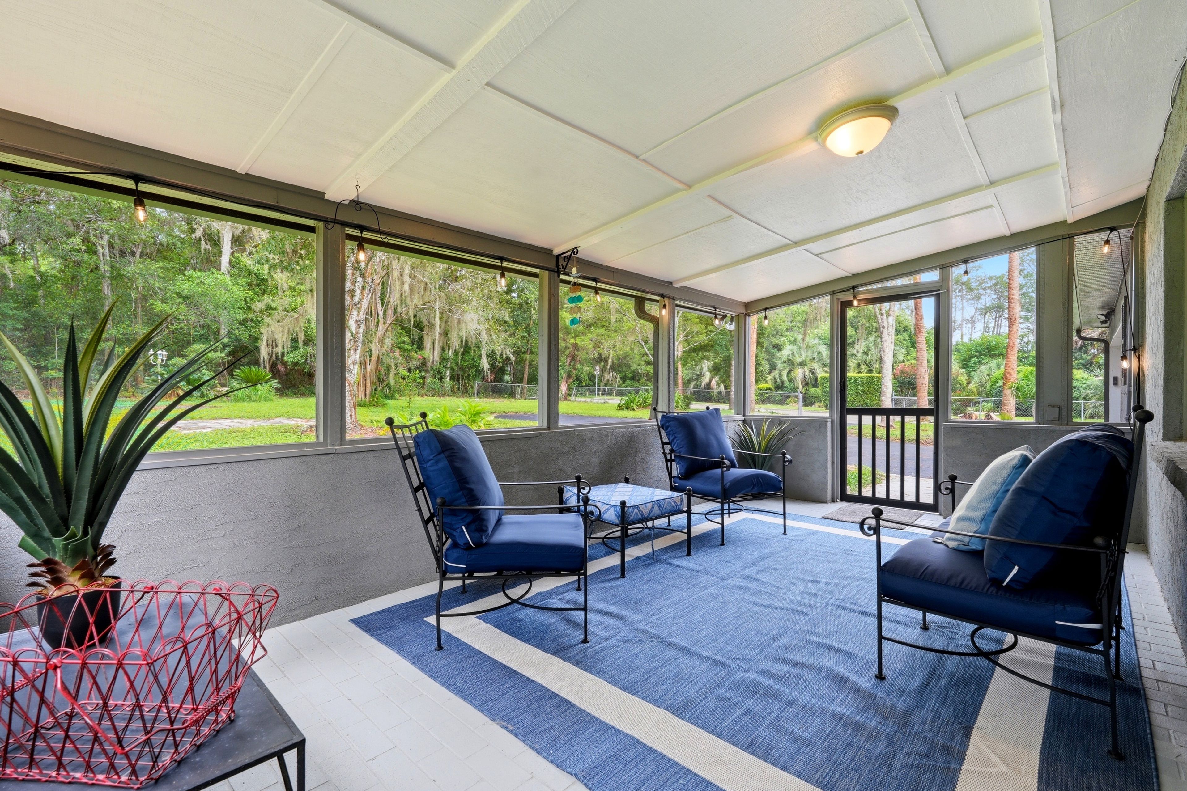 A covered patio area with a blue and white striped rug, metal-framed chairs, and a red metal table.