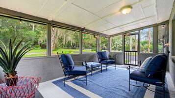 A covered patio area with a blue and white striped rug, metal-framed chairs, and a red metal table.