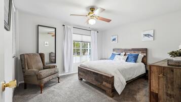 A bedroom with a wooden bed, a chair, a ceiling fan, and a window with curtains.