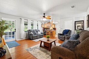 Ein großzügiges Wohnzimmer mit einer Couch, Sesseln, einem Couchtisch und einem Essbereich, im Hintergrund ist eine Küche zu sehen.