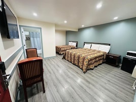 Habitación de hotel con dos camas, un escritorio, una silla, un televisor y una kitchenette pequeña.