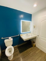 Un baño con inodoro blanco, lavamanos con espejo y pared azul.