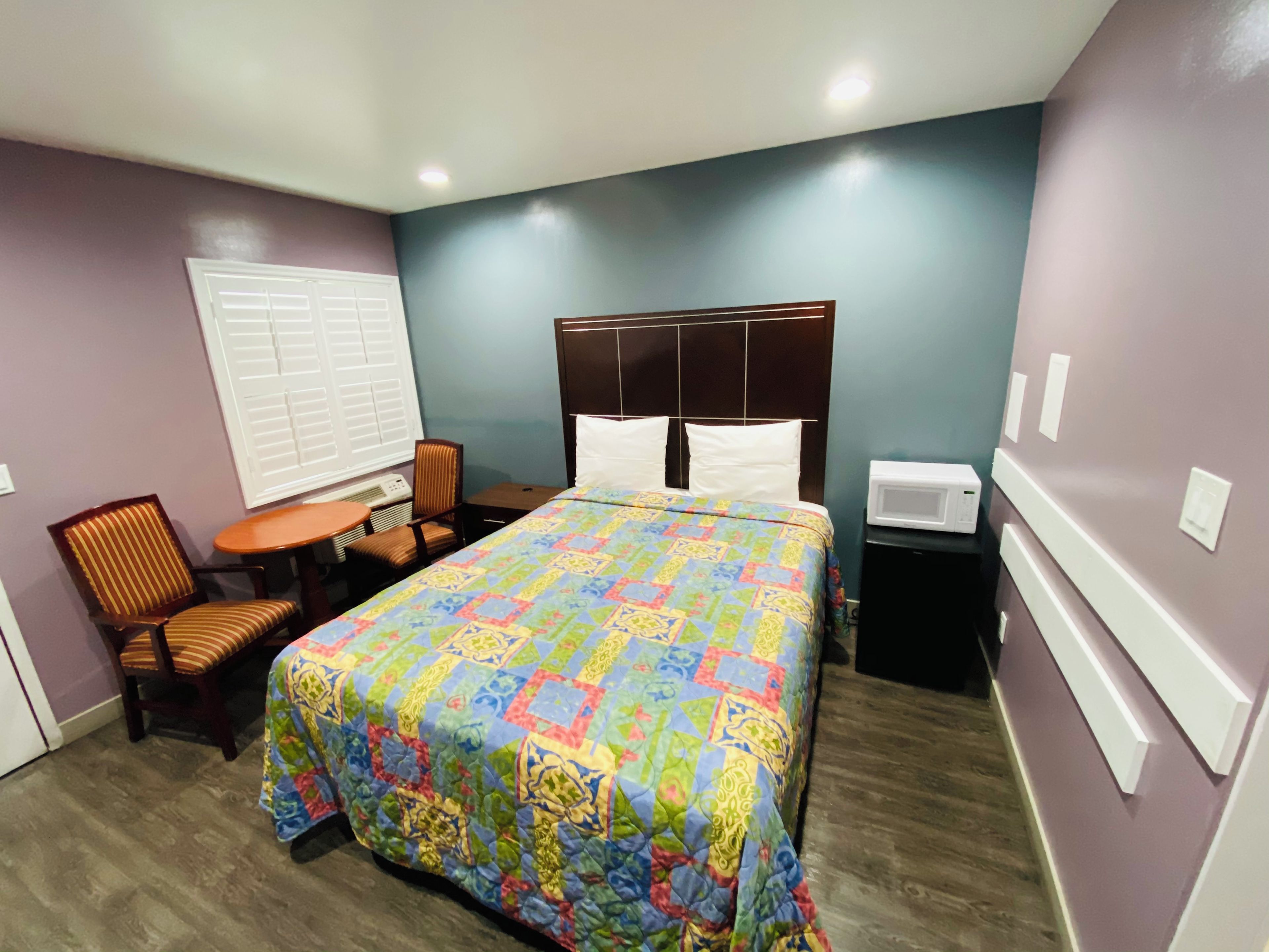 Quarto de hotel com cama, cadeira, mesa e micro-ondas.