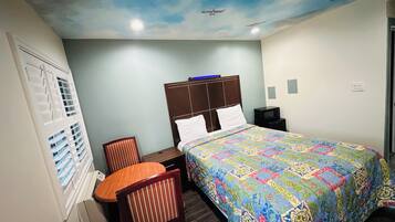A hotel room with a bed, a desk, a chair, a television, and a ceiling mural.