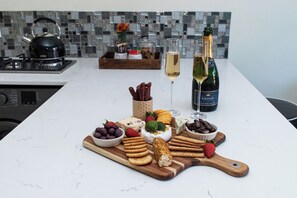 Eine Küchenarbeitsplatte mit verschiedenen Speisen und Getränken, darunter Käse, Cracker und eine Champagnerflasche.