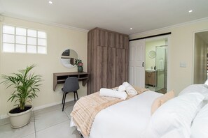 A hotel room with a bed, a desk, a chair, a potted plant, and a wardrobe. - Comfortable Living within walking distance to go swim, surf, dine or just relax (Cape Town)