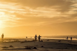 A beach scene with people walking and standing, and a sunset in the background. - Comfortable Living within walking distance to go swim, surf, dine or just relax (Cape Town)