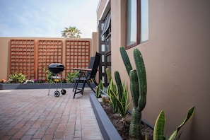 Eine Terrasse mit Grill, Stuhl und Kakteen.