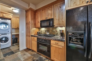 Una cocina con armarios de madera, un refrigerador de acero inoxidable, un microondas, una estufa y una lavadora.
