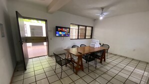 A room with a tiled floor, a wooden table with chairs, a television mounted on the wall, and a ceiling fan. - Tzalahua House (Manzanillo)