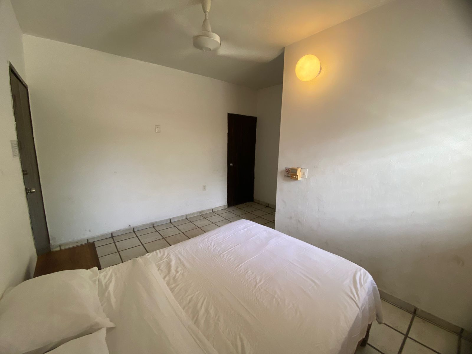 Una habitación con cama, puerta, lámpara y ventilador de techo.