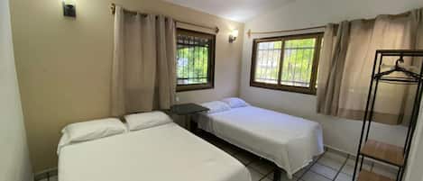 A room with two beds, a ceiling fan, a window with curtains, and a clothing rack.