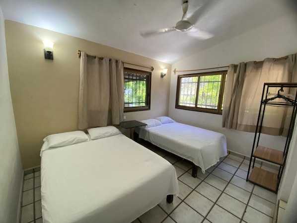 Ein Zimmer mit zwei Betten, einem Deckenventilator, einem Fenster mit Vorhängen und einem Kleiderständer.