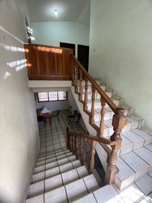 Eine Treppe mit Holzbalkonen führt zu einer Empfangsebene mit Tisch und Stühlen.